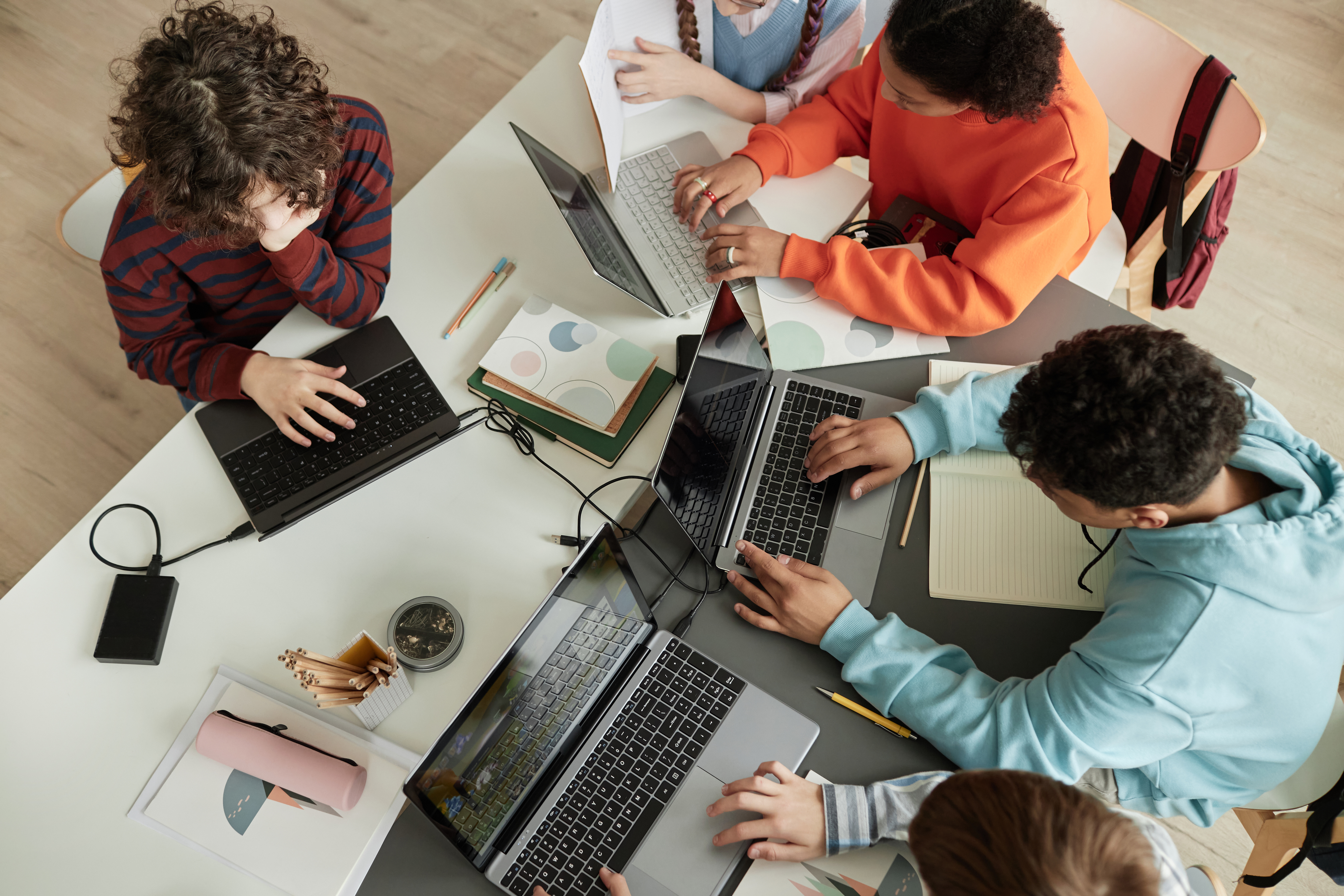 Top view at diverse group of teen school children using computers in classroom studying together at table